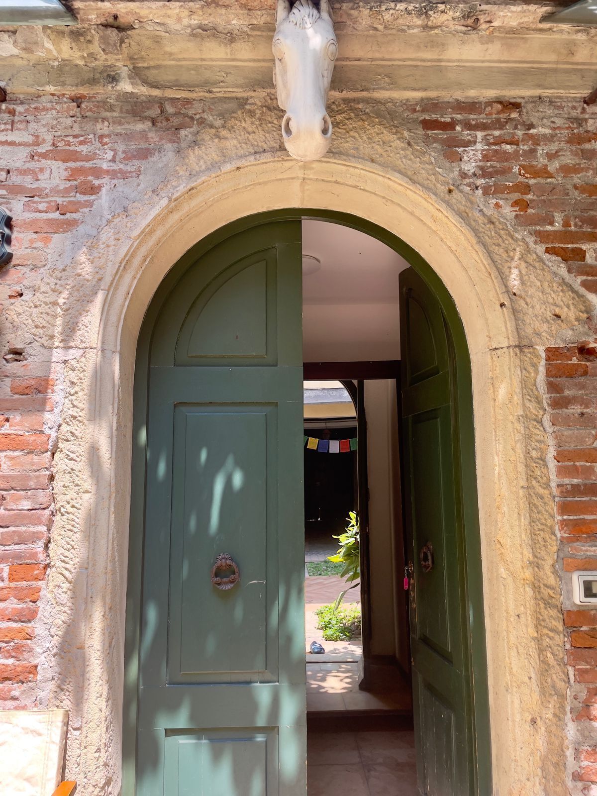 An arched doorway with a green door, leading to a brick interior.