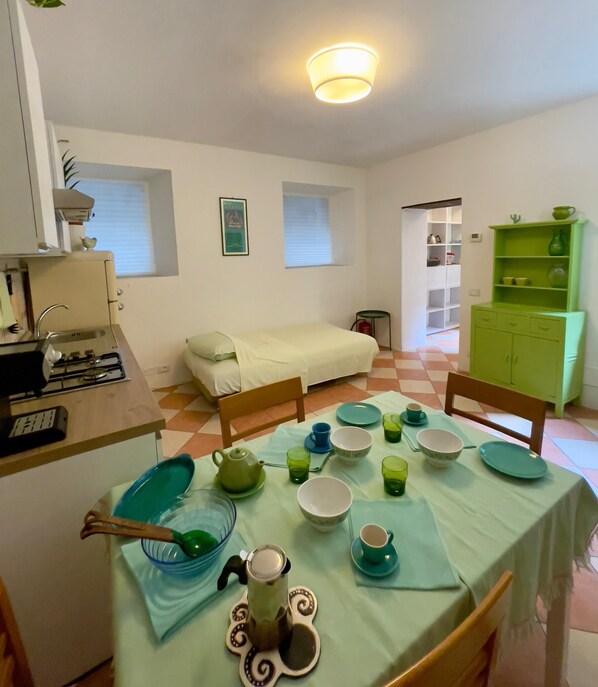 A compact living space with a kitchenette, a dining area with a table set for tea, a sofa, and a green cabinet.