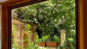 A view through a window of a courtyard with a brick wall, potted plants, and a pathway. - Detached apartment in seventeenth-century building with indoor garden. (Verona)