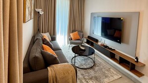 A modern living room with a sofa, armchairs, a coffee table, and a TV. - 1-Bedroom Pool View Unit @Nova (Accra)