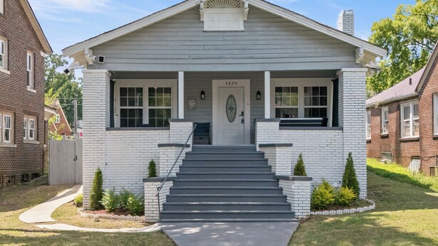 Une maison à deux étages avec un porche à l’avant, le numéro « 1330 » au-dessus de la porte et un petit jardin agrémenté d’arbustes.