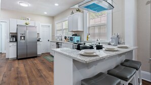 Une cuisine moderne avec des meubles blancs, un réfrigérateur en acier inoxydable, un four à micro-ondes encastré et un grand îlot central doté de tabourets de bar.