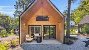 A wooden cabin with a pitched roof, large sliding glass doors, and a patio area with seating.