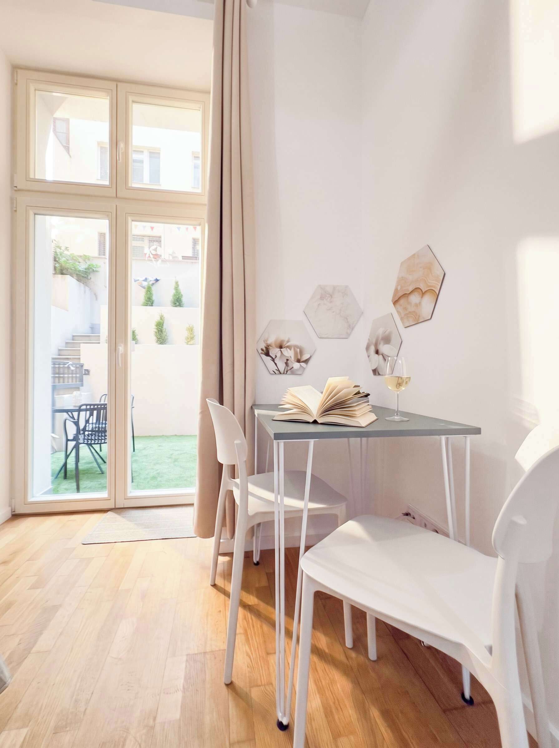 Un comedor moderno con una mesa de vidrio, sillas blancas y vistas a un jardín a través de ventanas amplias.