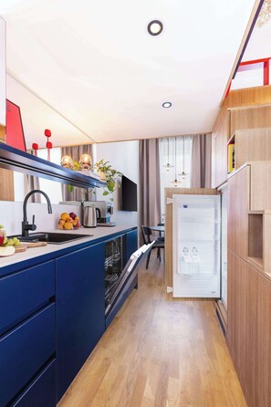 Une cuisine compacte comprenant un évier, une cuisinière et un réfrigérateur, des placards en bois et un coin repas avec une table et des chaises.