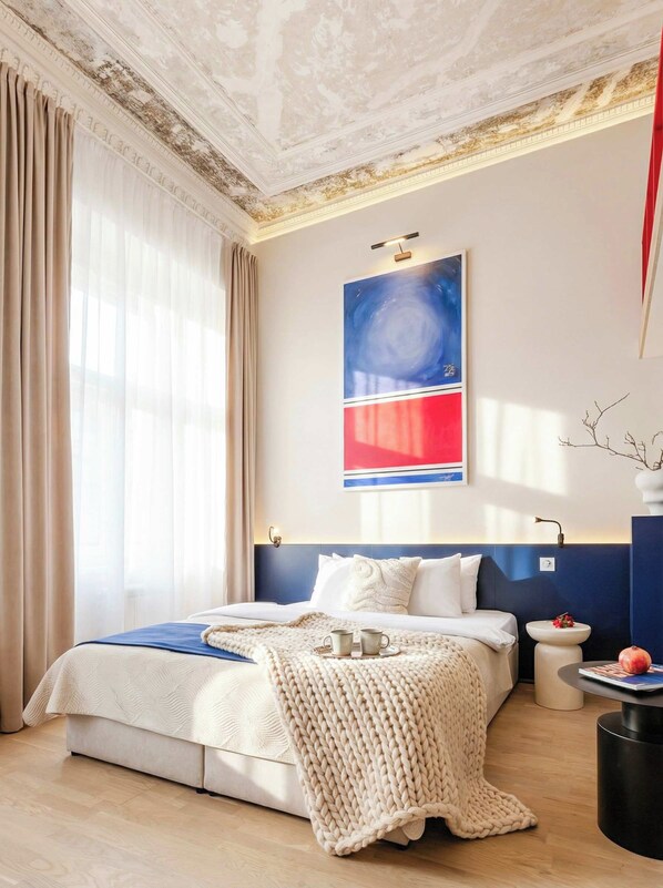 A bedroom with a bed, a large abstract painting, a bedside table, and a potted plant.