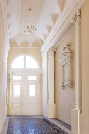 Un vaste hall d’entrée doté d’une double porte, d’un lustre et de détails architecturaux classiques.