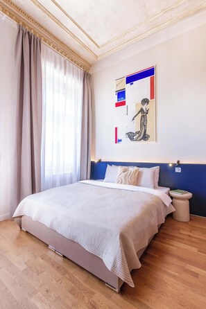 Une chambre d’hôtel avec un grand lit, une tête de lit agrémentée d’une touche de bleu, une table de chevet avec une lampe et une œuvre d’art accrochée au mur.