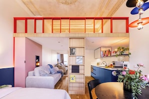 Une chambre d’hôtel moderne avec un lit en mezzanine, un canapé, une table à manger et un coin cuisine.