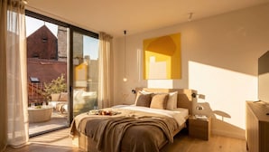 A modern bedroom with a large bed, a bedside table, a nightstand, a TV, and a view of a cityscape through a sliding glass door. - TurnKey | Henry's Tower Studio with Terrace III-3 (Hlavní město Praha)