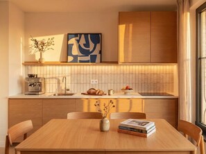 A modern kitchen with wooden cabinets, a countertop, a coffee machine, and a dining table with chairs. - TurnKey | Henry's Tower Apartment III-4 (Hlavní město Praha)