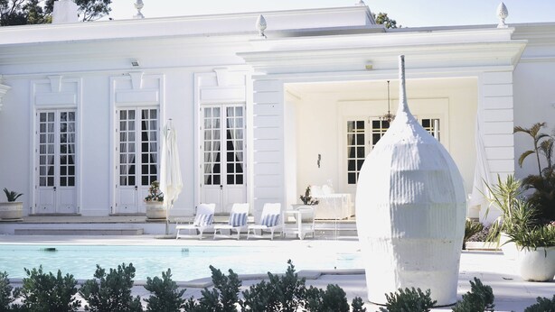 Un edificio blanco con piscina, sillas de descanso y una fuente.