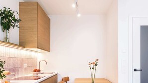 A modern kitchen with wooden cabinetry, a white countertop, and a dining area with a wooden table and chairs. - TurnKey | Henry's Tower Apartment IV-2 (Hlavní město Praha)