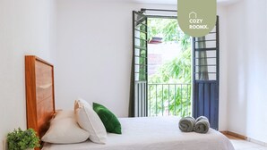 A bedroom with a bed, pillows, a small plant, and a balcony with a view of greenery. - 3 BDR Apt/Private Terrace/ Pet F/Parking/100MB (Oaxaca de Juárez)