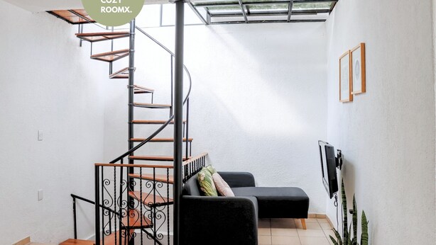A compact living space with a spiral staircase, a black sofa, a TV, and a plant. - 3 BDR Apt/Private Terrace/ Pet F/Parking/100MB (Oaxaca de Juárez)