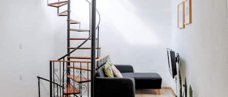 A compact living space with a spiral staircase, a black sofa, a TV, and a plant.