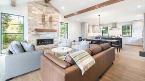 A modern living room with a stone fireplace, a large sofa, and a dining area with a kitchen in the background.