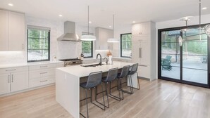 A modern kitchen with a large island, bar stools, and a view of the outdoors.