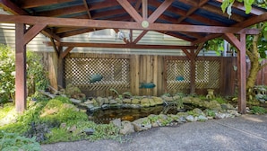 A wooden pergola with a pond, surrounded by rocks and plants.