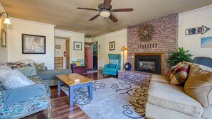 A living room with a fireplace, a ceiling fan, and a brick accent wall.