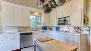 A modern kitchen with white cabinets, a stainless steel dishwasher, a wooden table, and a window providing natural light.