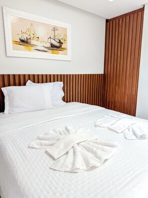 A neatly made bed with white linens and towels, a wooden headboard, and a painting of a boat on a river. - Hotel Glória (Piranhas)