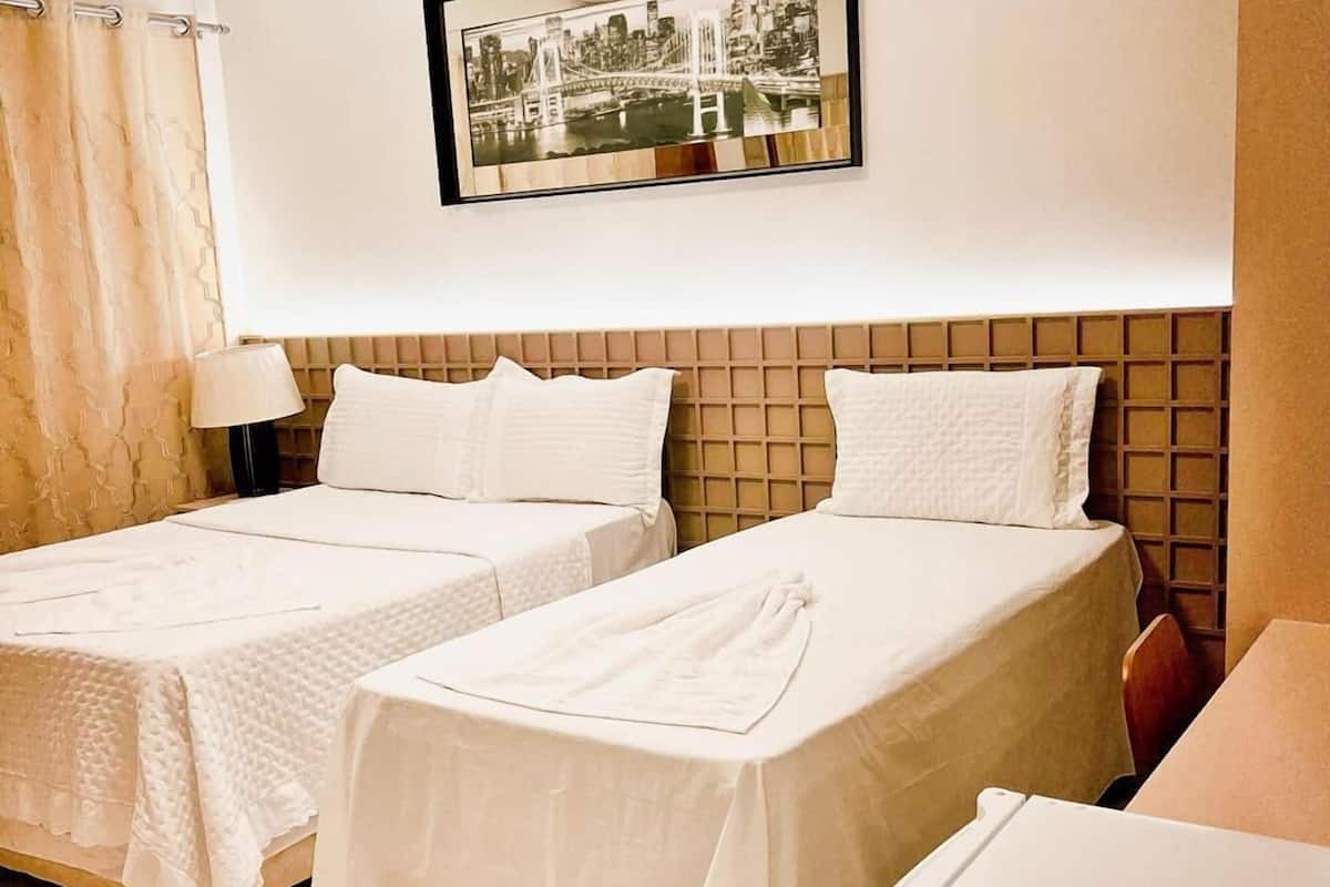 A hotel room with two beds, a small desk, a nightstand, a lamp, and a framed picture on the wall.