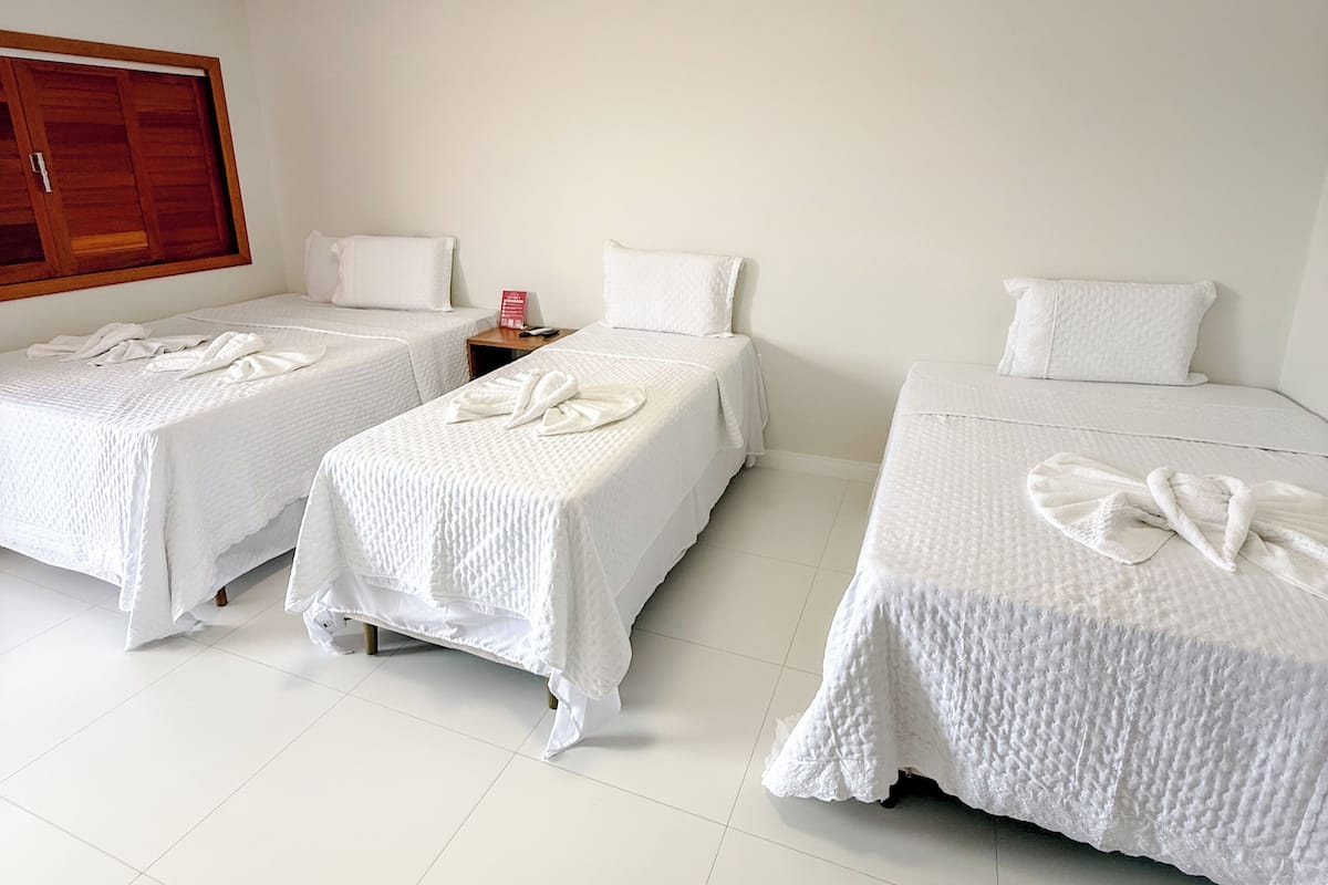 A hotel room with three single beds, a wooden wardrobe, a nightstand, and a ceiling light.