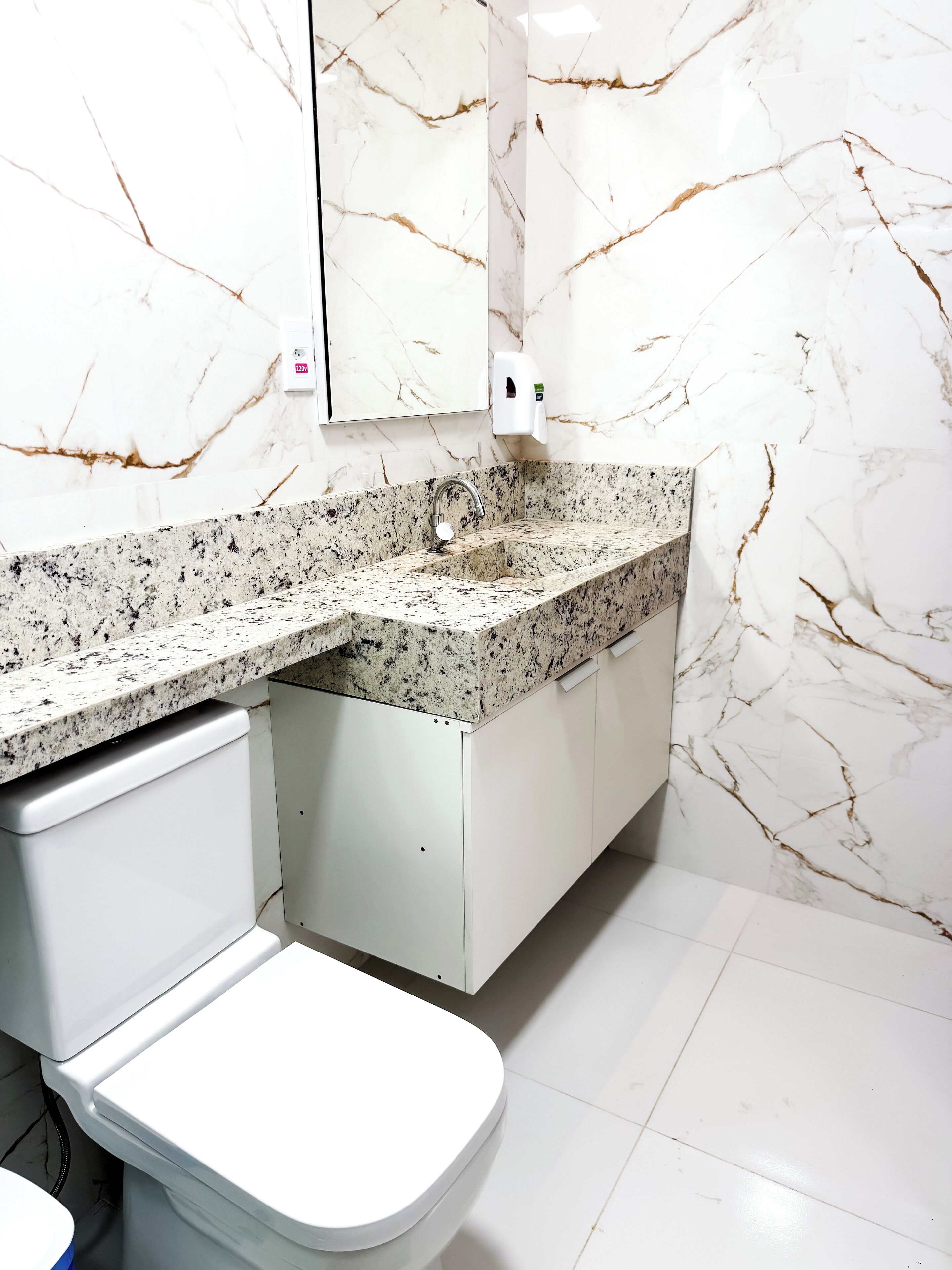 Une salle de bain avec des toilettes blanches, un pare-feu en marbre et un comptoir en granit.