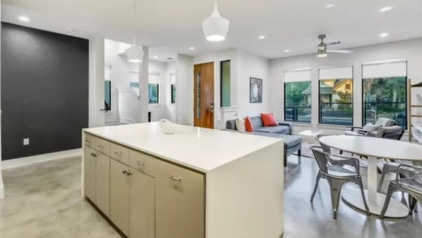 A modern kitchen with a central island, a dining area with a round table and chairs, and a living space with a sofa and a coffee table. - Cityscape Retreat | Sleeps 14 | City Views + Grill (Austin)
