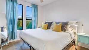 A bedroom with a large bed, a bedside table with a lamp, and a window with curtains. - Cityscape Retreat | Sleeps 14 | City Views + Grill (Austin)