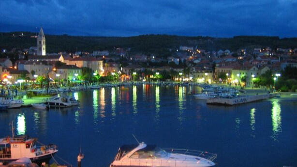 Uma marina com barcos atracados, uma torre imponente e uma cidade ao fundo, com edifícios e luzes.
