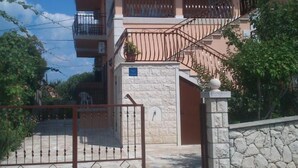 Um edifício residencial de vários andares com fachada de pedra, entrada fechada por portão e varanda com grade de metal.