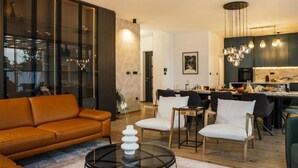 A modern living room with a leather sofa, a glass coffee table, and a dining area with chairs and a kitchen in the background.