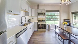 Una cocina moderna con armarios blancos, electrodomésticos de acero inoxidable y una mesa de madera con bancos.