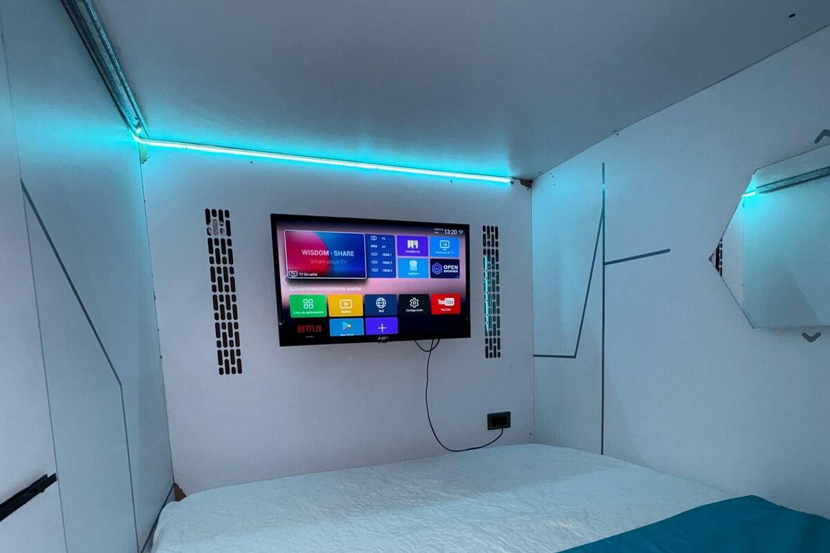 A modern hotel room with a bed, a mounted TV displaying various apps, and a blue accent wall.
