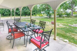 Eine überdachte Terrasse mit Tisch und Stühlen, umgeben von einem Garten und Blick auf eine Wohnstraße.
