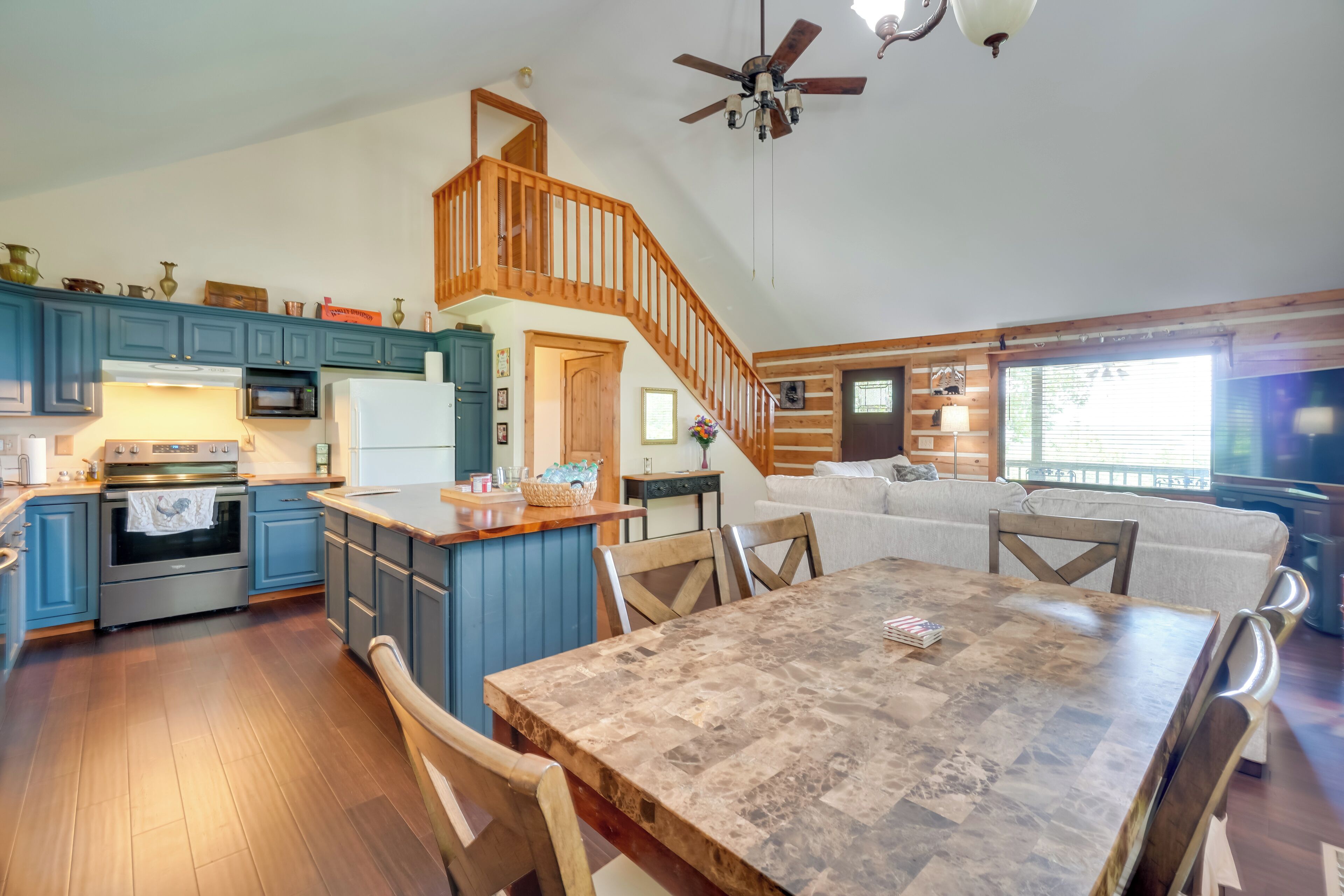 A spacious kitchen with blue cabinets, a wooden dining table, and a staircase leading to a loft bedroom.