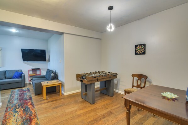 A living room with a foosball table, a TV mounted on the wall, and a dartboard.