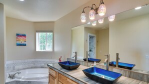 Une salle de bain avec une baignoire, deux vasques aux récipients bleus, un grand miroir et une fenêtre donnant sur la forêt.