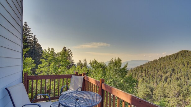 Une terrasse en bois avec une table et des chaises, donnant sur une colline boisée.