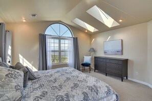 A bedroom with a large bed, a dresser, a chair, a skylight, and a window with curtains.
