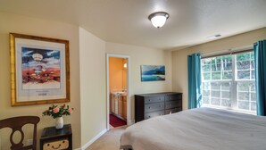 Une chambre à coucher avec un grand lit, une commode, une chaise, un tableau encadré et une fenêtre avec des rideaux.
