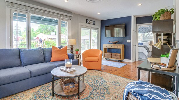Een woonkamer met een blauwe bank, een oranje fauteuil, een ronde salontafel en een tapijt met een patroon.