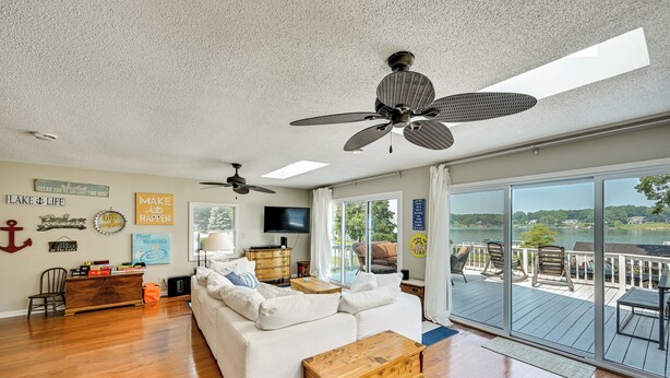 A spacious living room with a white sofa, wooden coffee table, and ceiling fans. There is a large window offering a view of the outdoors. - Dock & Kayaks: Lake-View Home, 29 Mi to Notre Dame (Union)