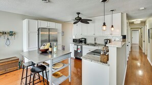 A modern kitchen with white cabinetry, a stainless steel refrigerator, a microwave, and a built-in oven. There is a wooden island with stools, and pendant lights hang above the island. - Dock & Kayaks: Lake-View Home, 29 Mi to Notre Dame (Union)