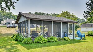 A screened porch with a covered seating area, surrounded by green plants and a small shed. - Dock & Kayaks: Lake-View Home, 29 Mi to Notre Dame (Union)