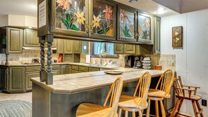 A kitchen with wooden cabinets, a large island with bar stools, and a window with a view of trees. - Beech Mt Lakefront Gem! Hot Tub, Kayaks, Billiards (Beech Mountain Lakes)