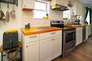 Una cocina con armarios blancos, electrodomésticos de acero inoxidable, encimera de madera y ventana con vistas.