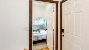 Un estrecho pasillo que conduce a un dormitorio con literas, una puerta con manija e interruptor de luz en la pared.
